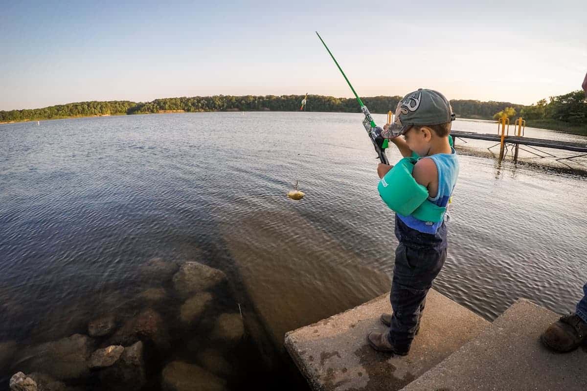 Little boy fishing off dock with floatation device on 