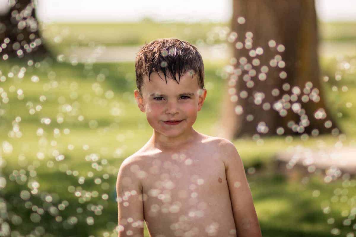 Boy surrounded by water sprinkler droplets 