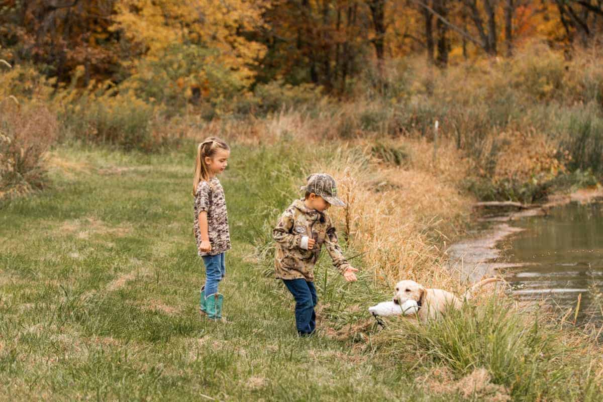 Boy and girl watch as dog comes out of pond with bumper