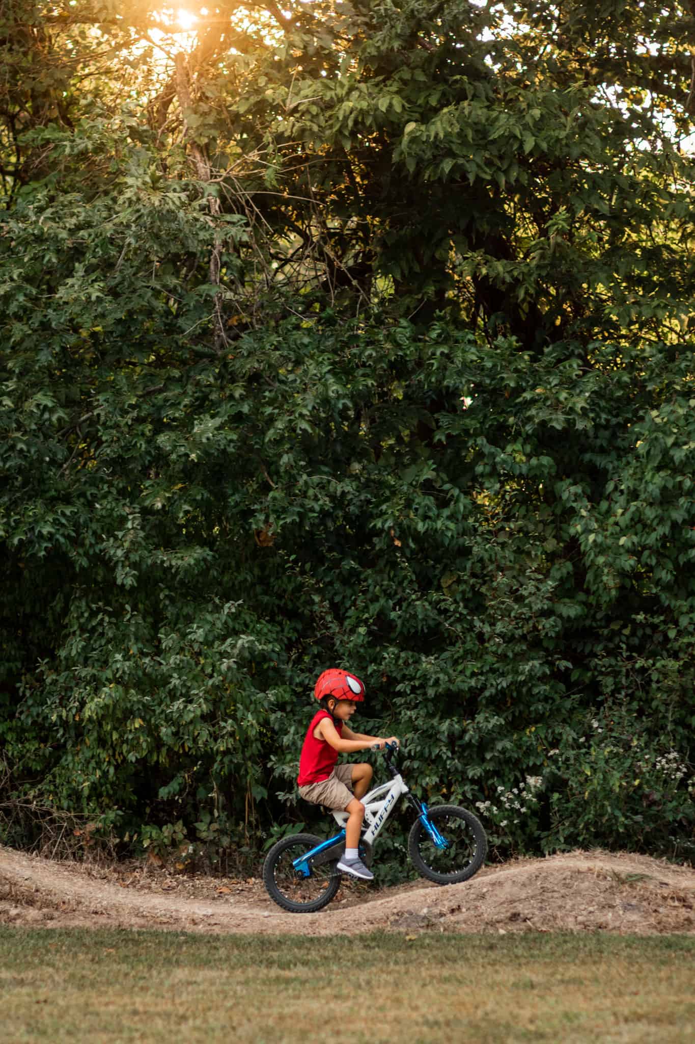 Child in red shirt and helmet riding bike over ramp