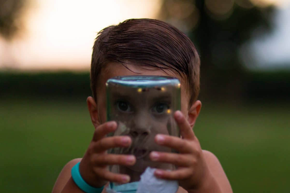 Boy holding mason jar with lightening bugs - backyard camping activities for kids