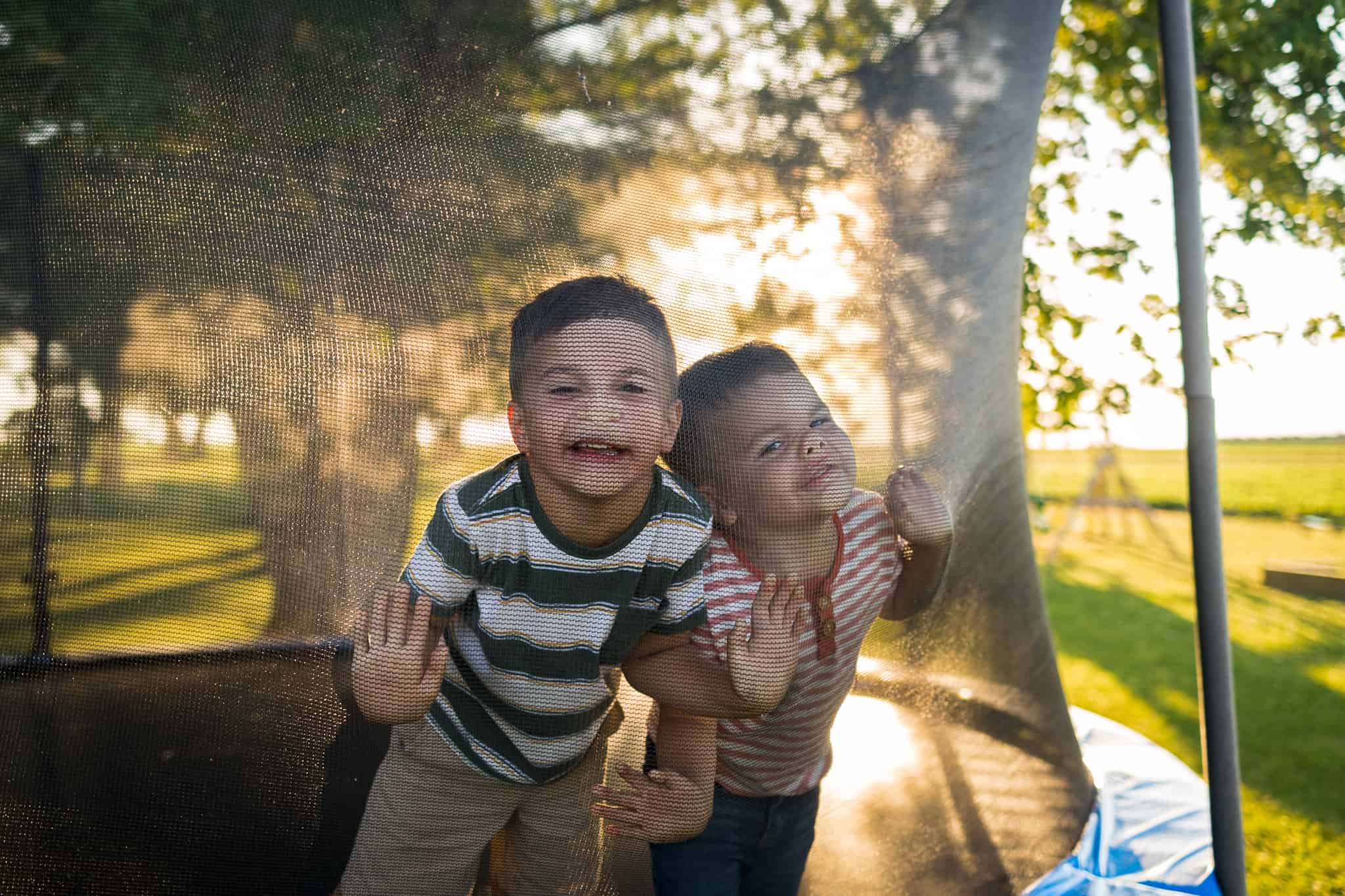 Two boys pressing their faces against trampoline netting 