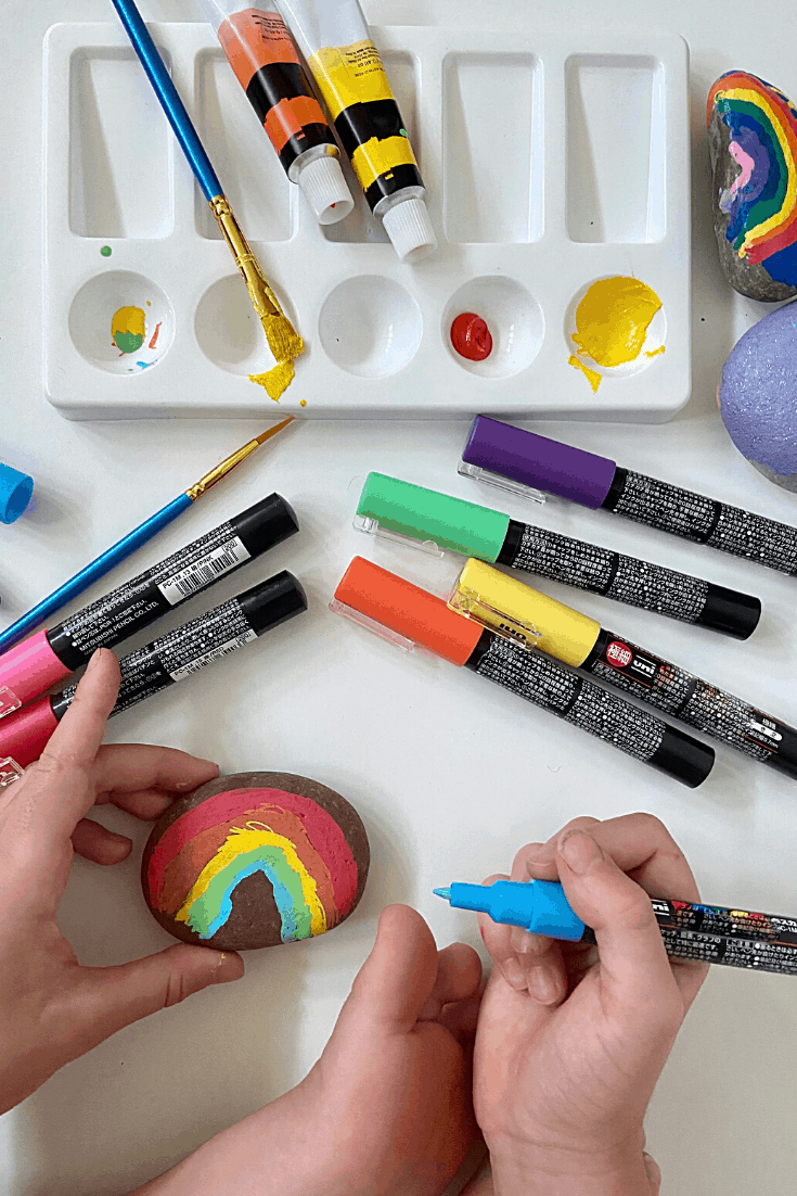 A child painting a rainbow on a rock with a paintpen