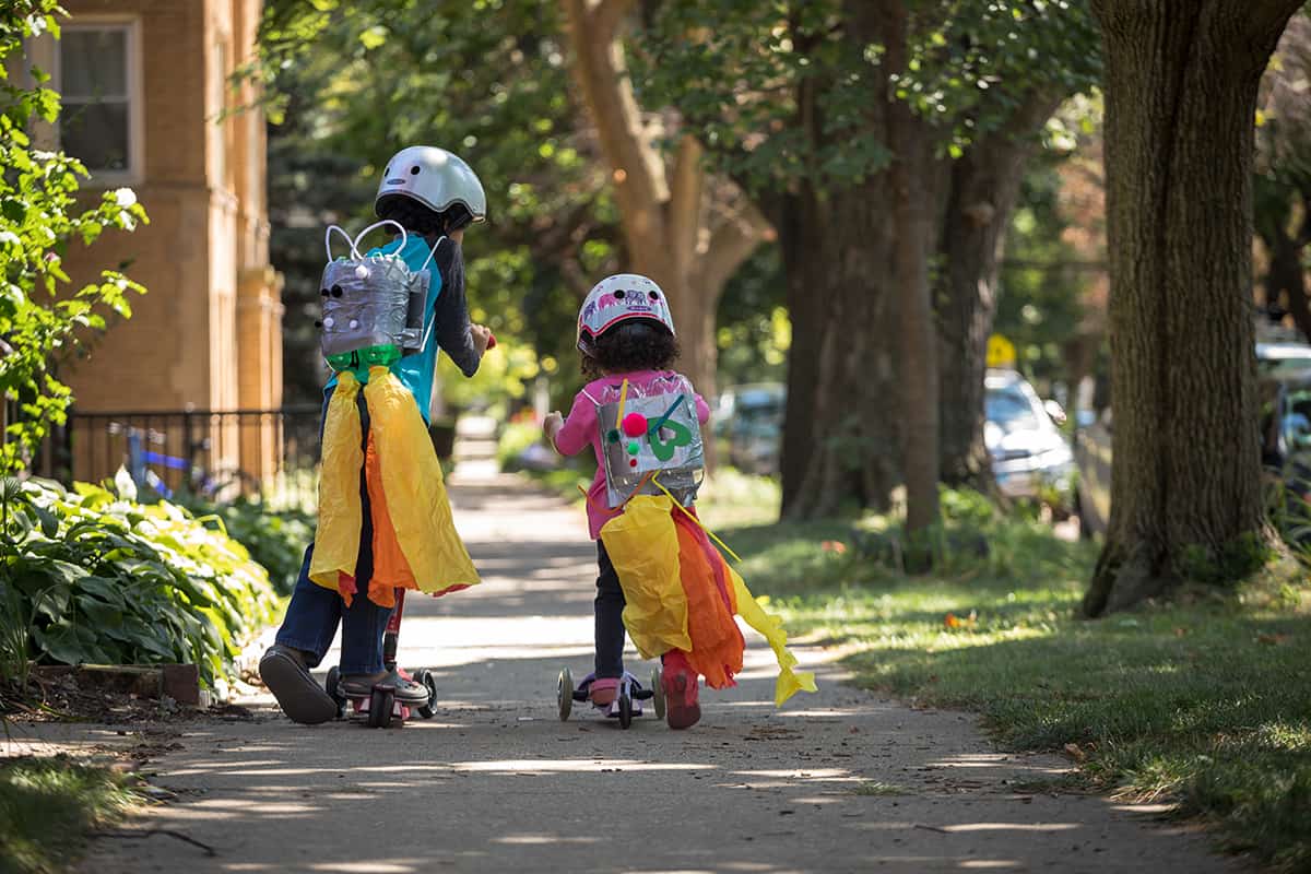 two kids on scooters on a sidewalk - urban nature with kids