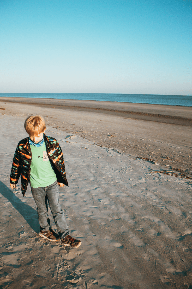 young boy walking in the sand at the beach during winter