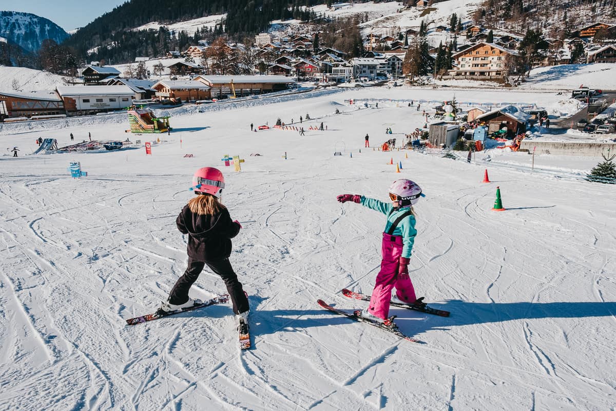 two kids stand on a ski slope where they are learning to downhill ski