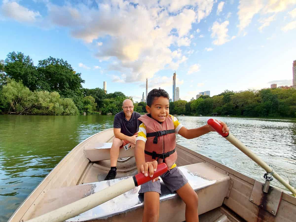 A boy rowing a boat at Central Park with his father