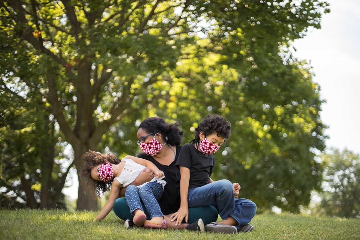 A mother and 2 children masked, playing outside.