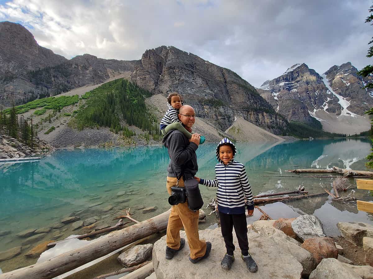 A dad with a camera standing at Lake Moraine in Banff with his two kids