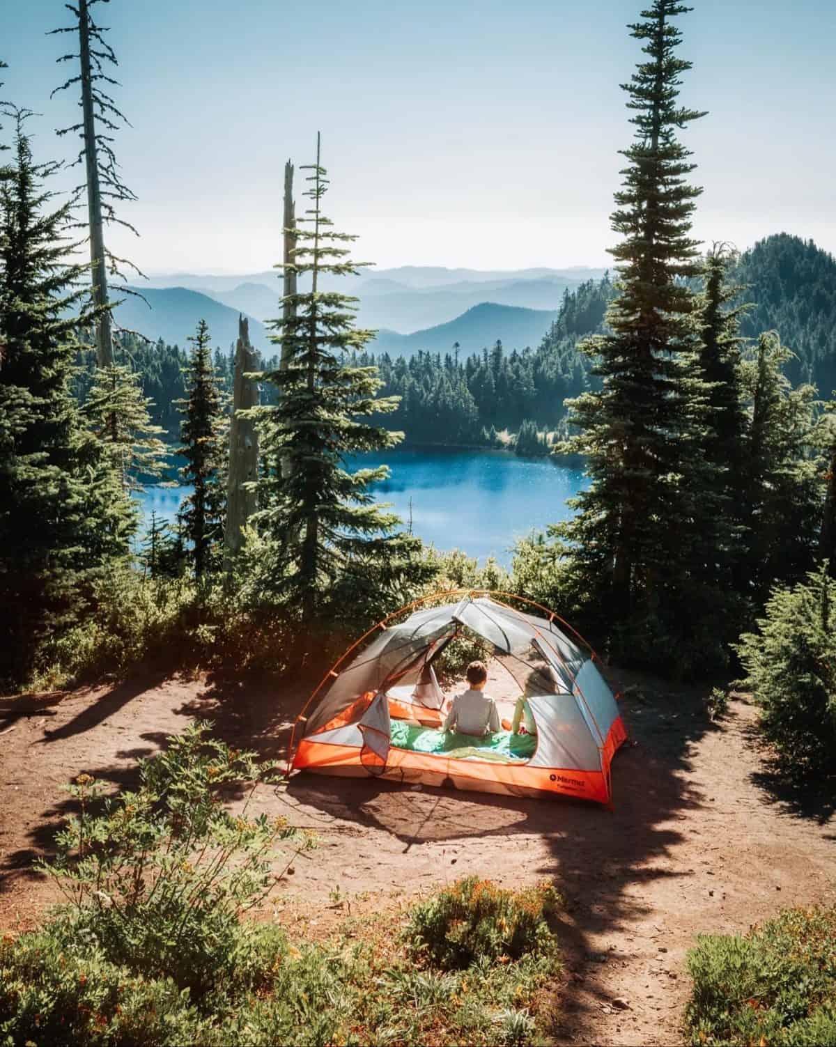 camping scene with tent among trees above a blue lake
