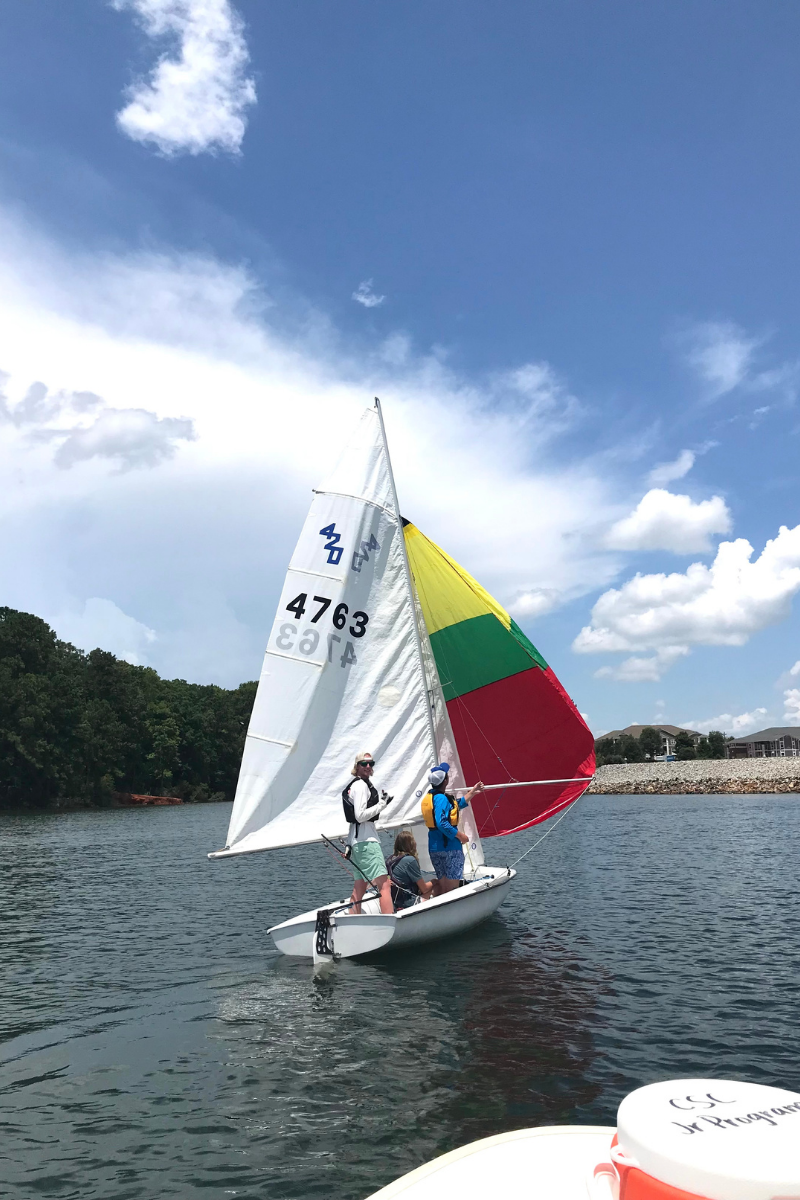 Colorful sailboat dinghy with instructors standing up giving advice to an unseen beginner sailor