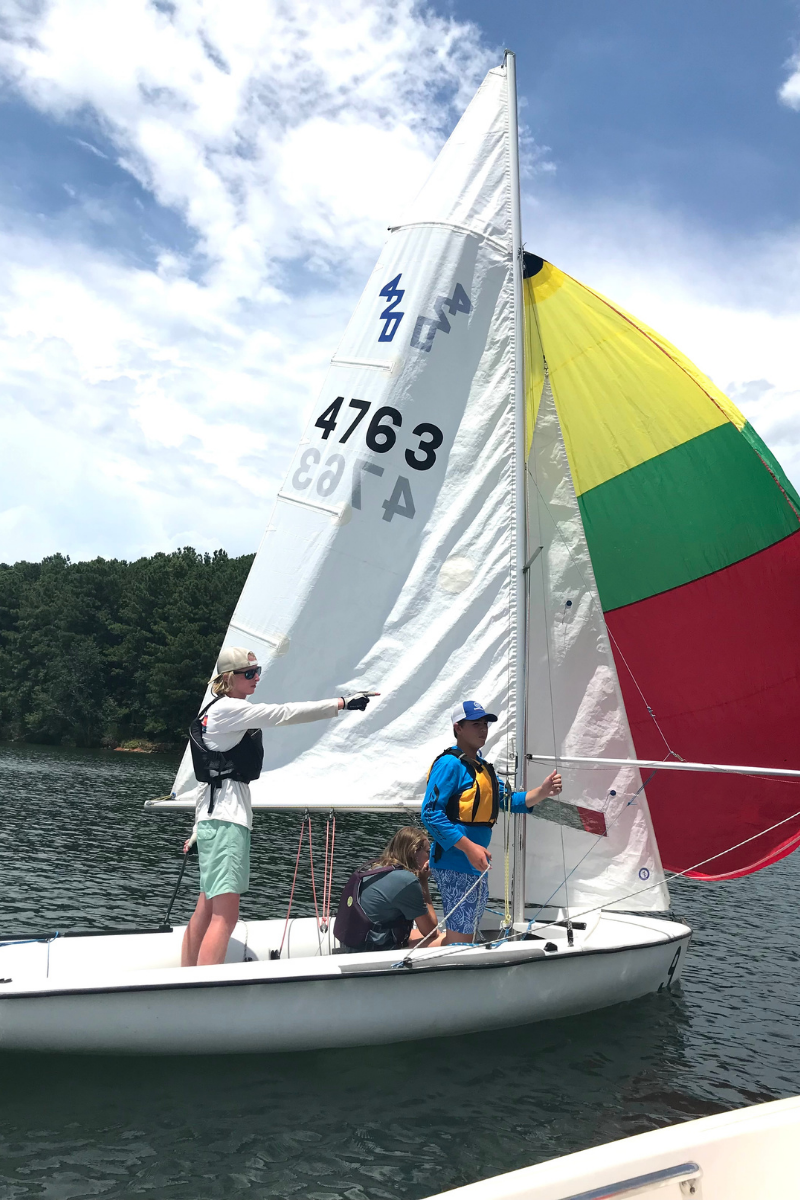 A sailing instructor standing in a dinghy pointing and giving instruction to an unseen beginner sailor