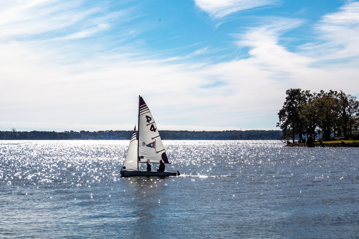 Single dinghy sailboat on a glistening clam lake and blue skies with wispy white clouds