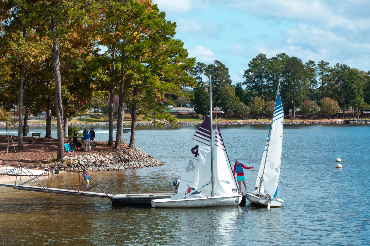 Two sailboats at the dock at a sailing club with trees in the background