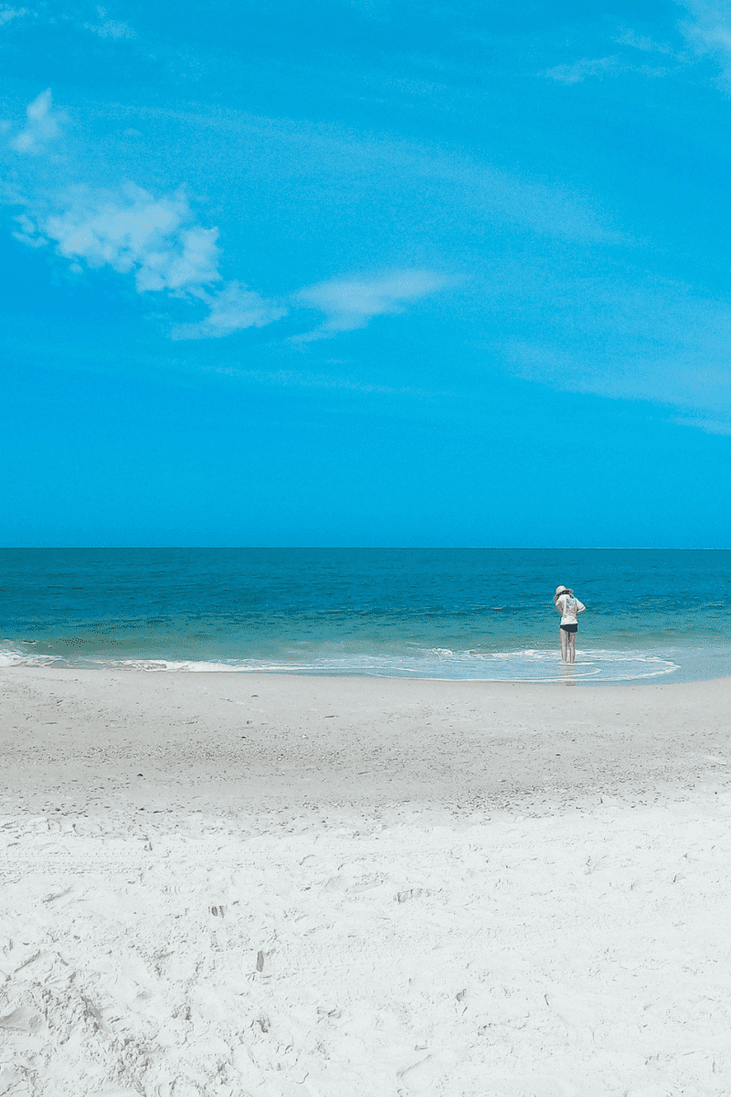 white sand beach with a teen girl with feet in the water of the gulf of mexico