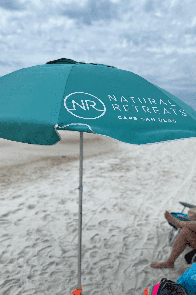 up close of a teal colored beach umbrella that reads Natural Retreats Cape San Blas