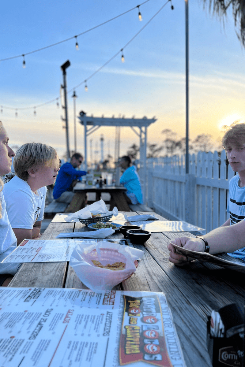 family eating outdoors with food and menus on the table, a sunset in the background