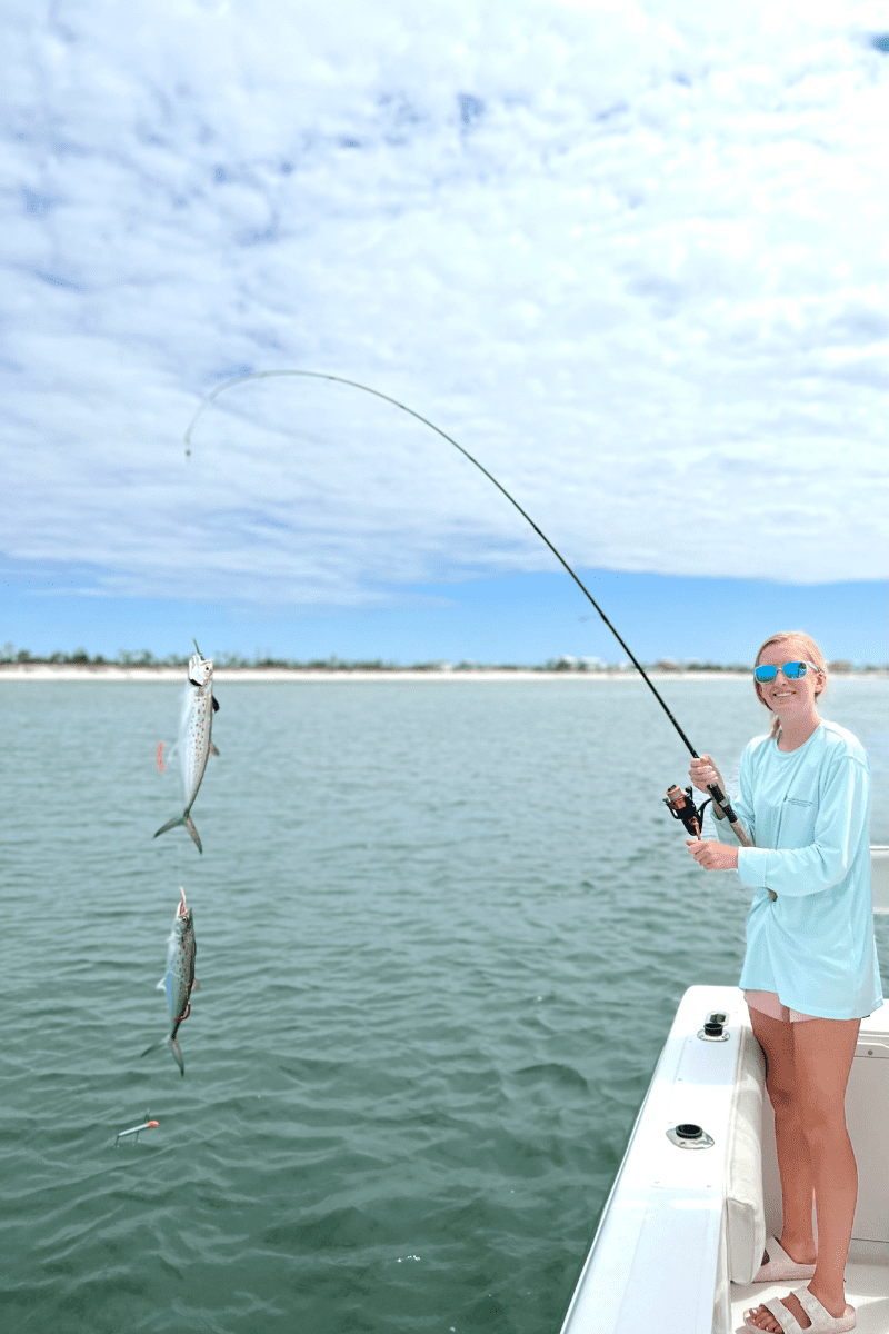 Teen girl with two fish hooked on a rod off the side of a fishing boat charter