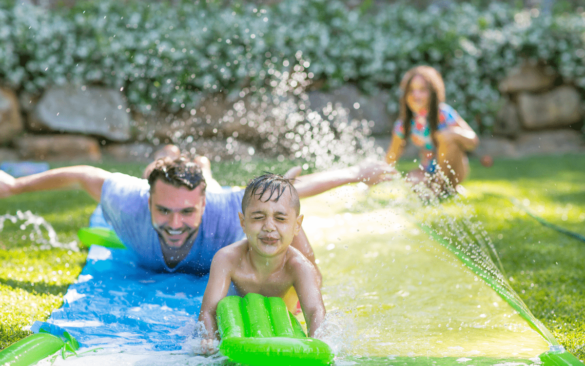 children and dad on slip n slide - best water toys, games and activities for kids
