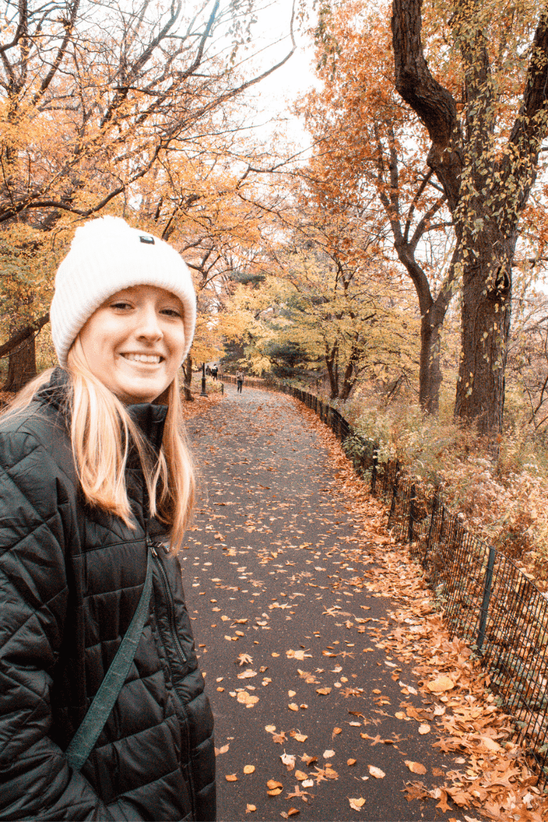 teen girl in central park in autumn with orange leaves on the trees and ground