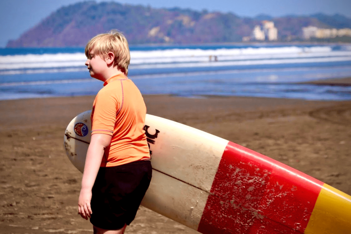 boy carrying a surfboard on a beach in Jaco, Costa Rica