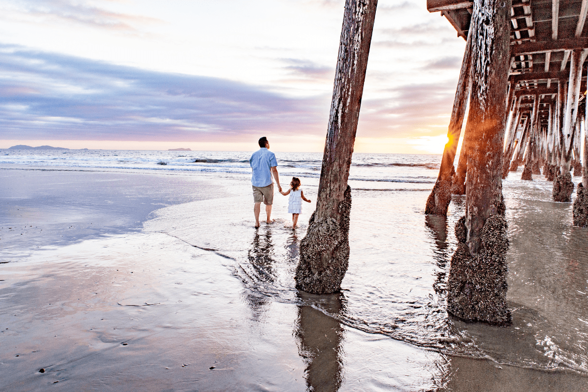 father and daughter walking hand in hand on the beach in san diego among trees on the shore line