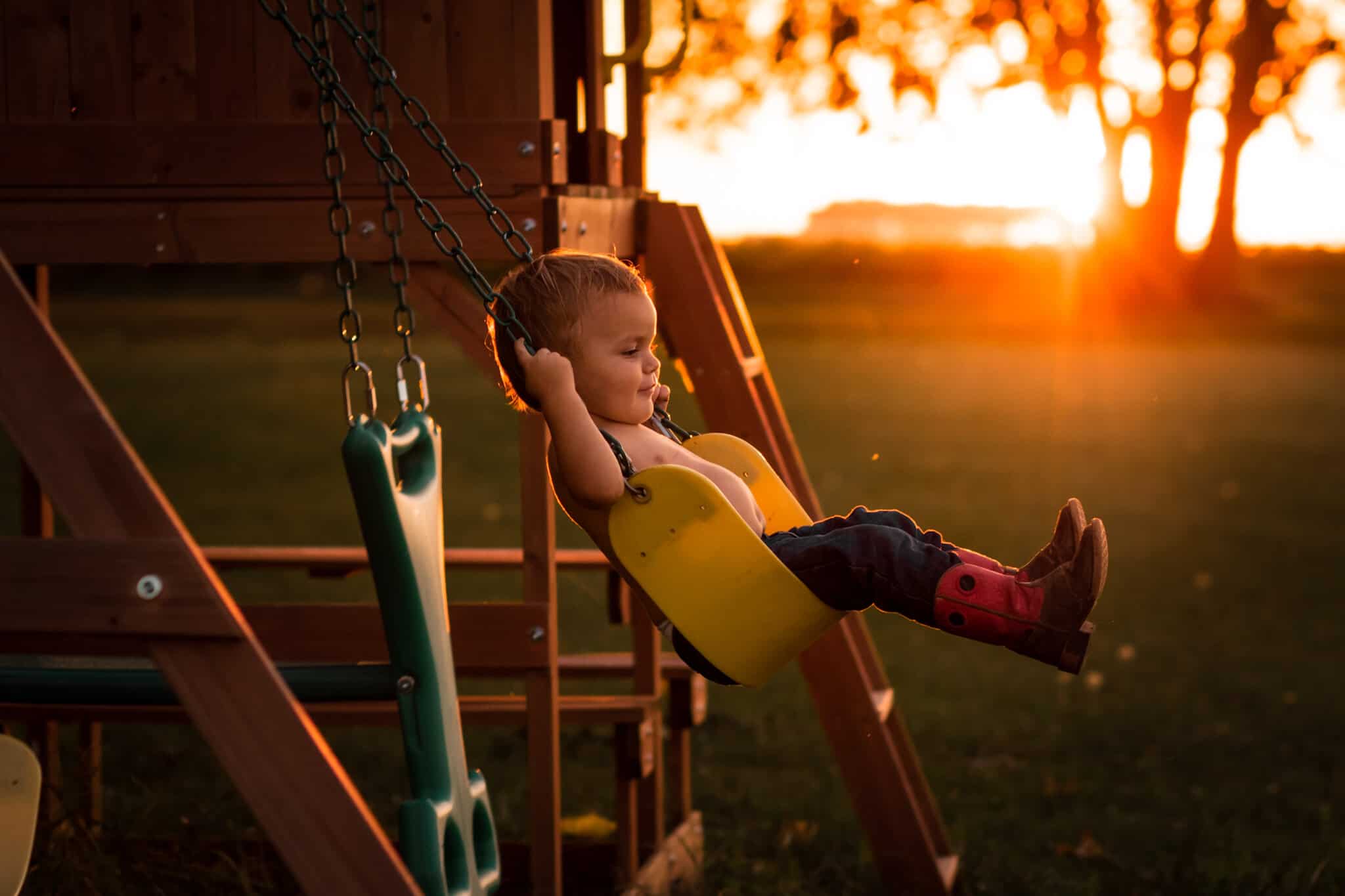 Child swinging on yellow swing at sunset 