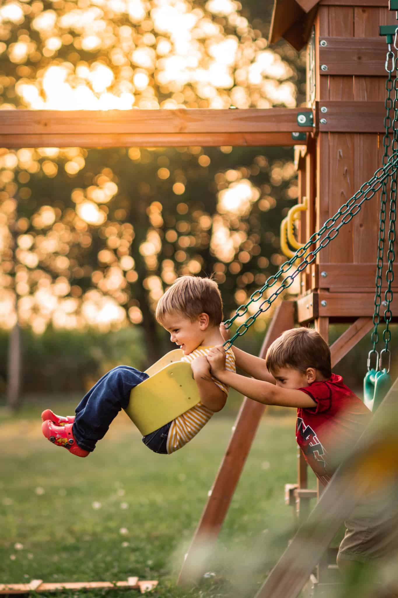 Boy in red pushing boy in yellow on a yellow swing