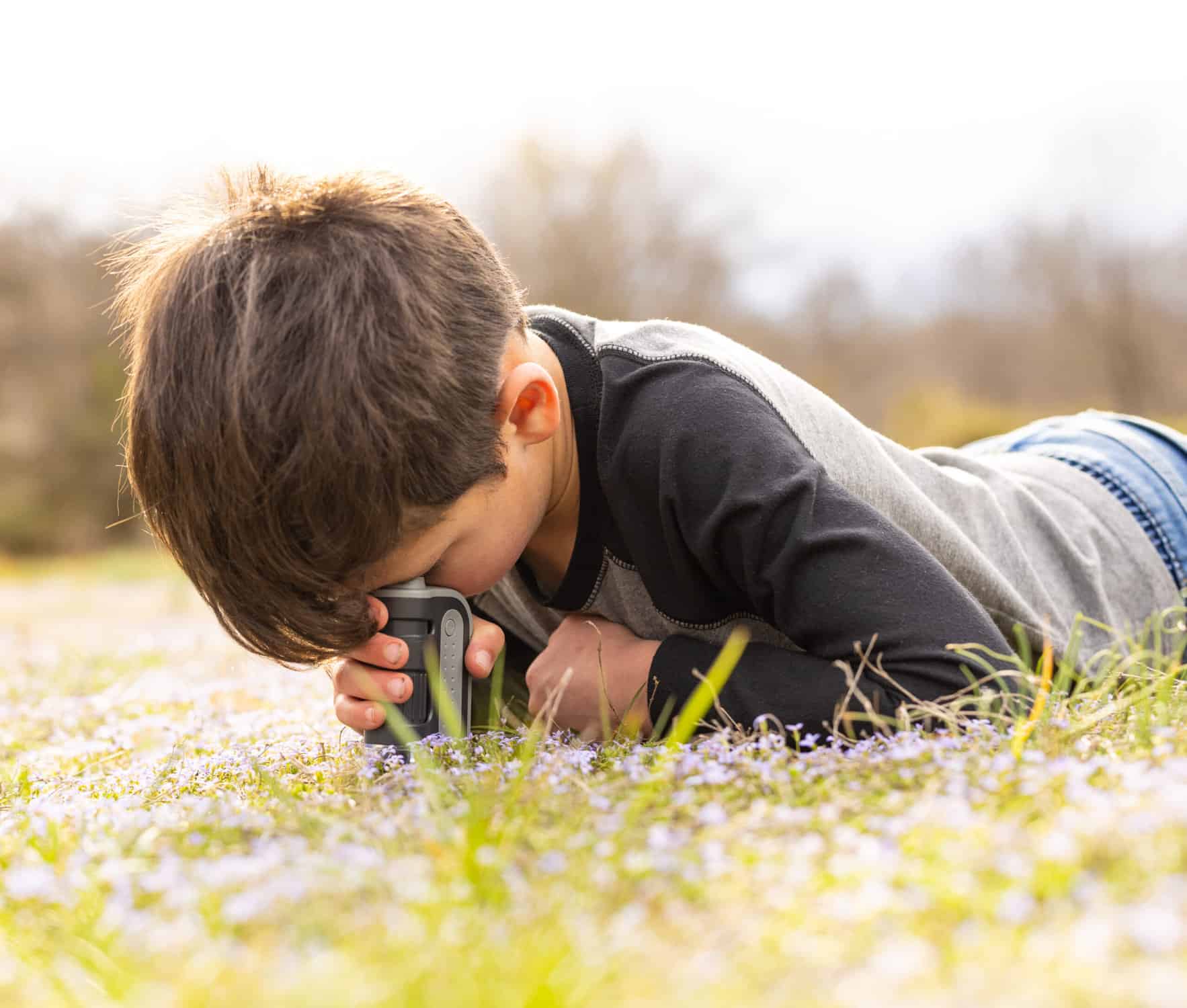 child laying in field looking at flowers with microscope