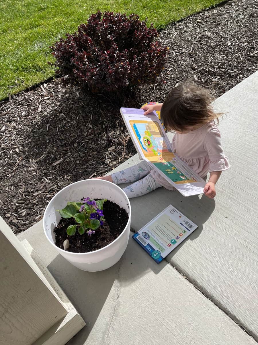 a child reading books outdoors next to some flowers