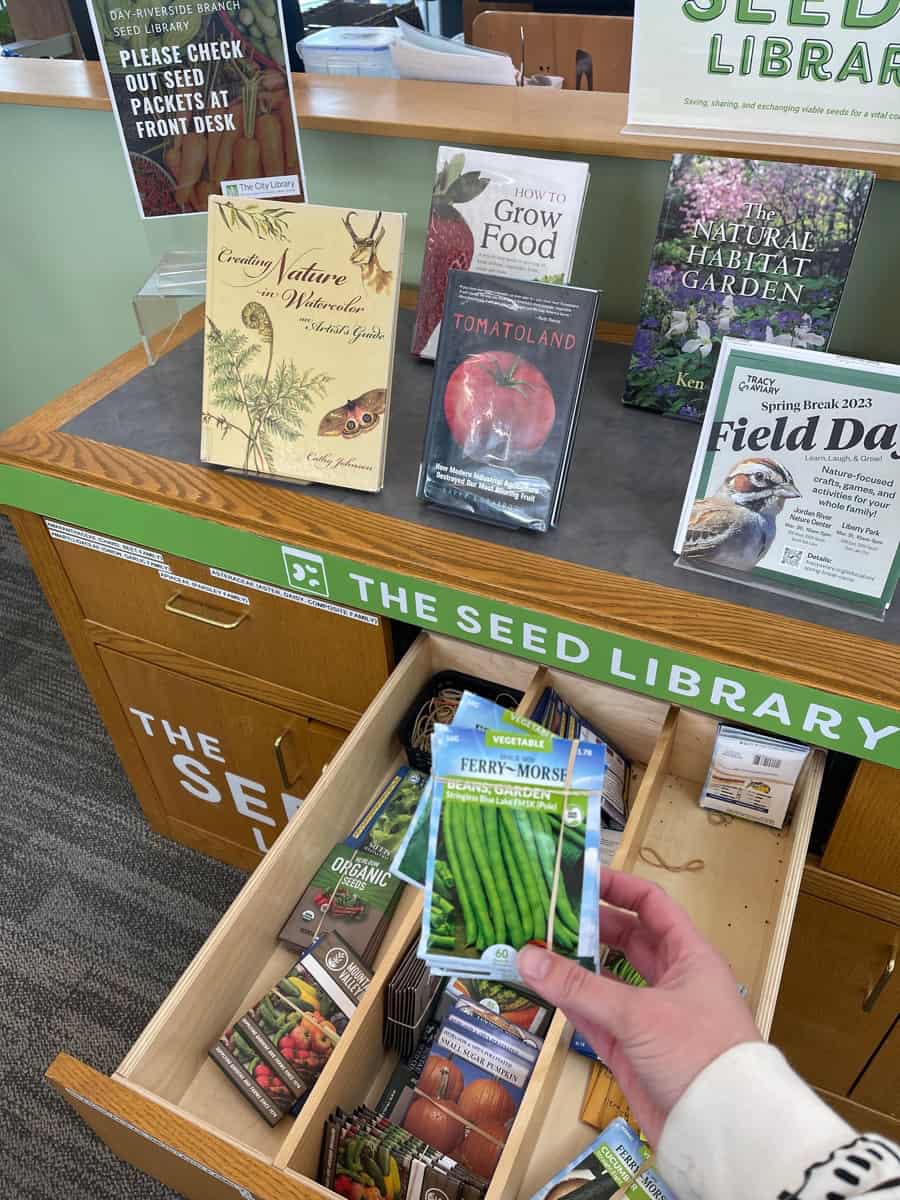 a library display of seeds. books about gardening and a packet of green bean seeds can be seen