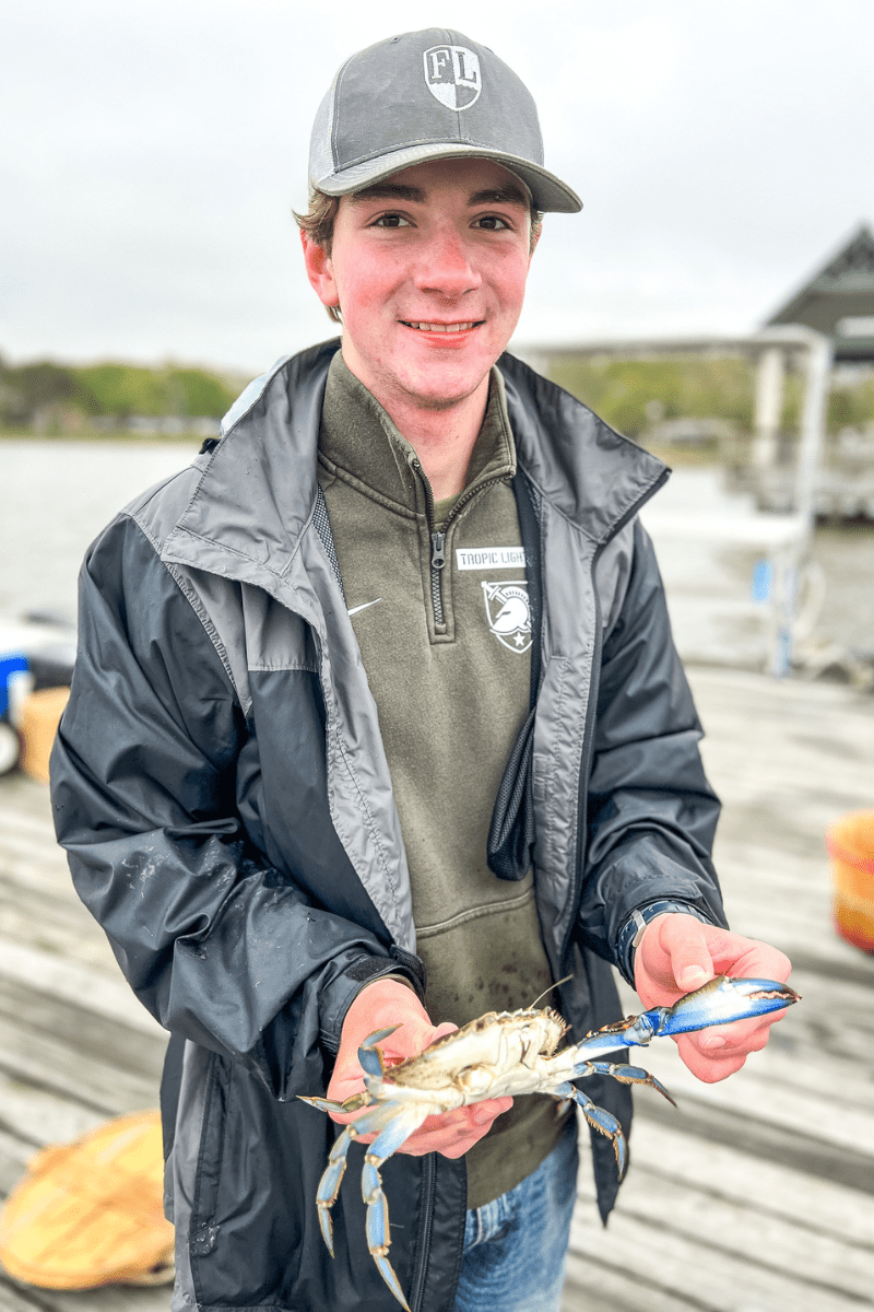 teen boy standing on a dock holding a one-claw crab 
