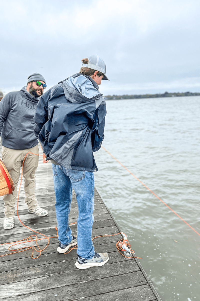 teen boy standing on a dock getting instructions from a pro on how to pull the rope line in with the crab basket