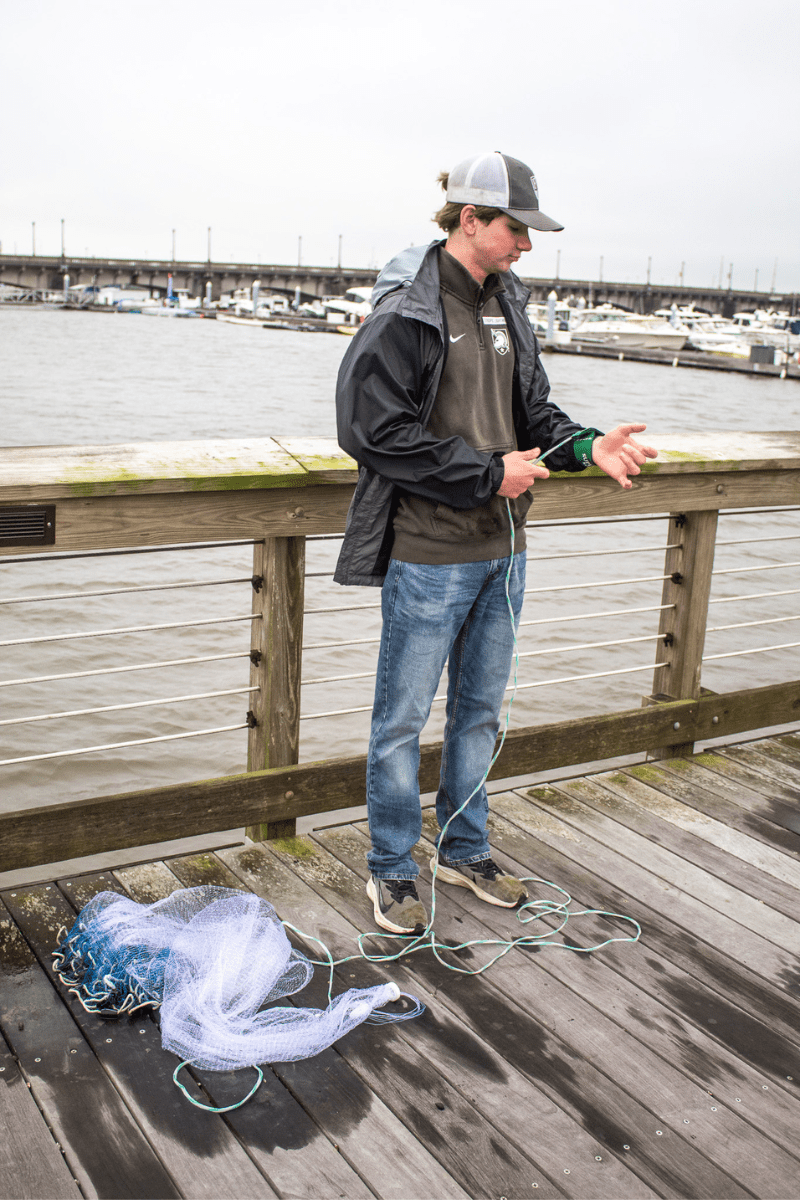 teen boy standing on a dock learning to tie a throw net to his wrist