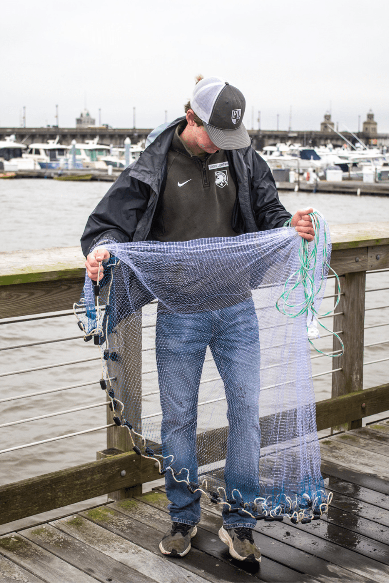 teen boy standing on a dock with a throw net in his hands checking his positioning