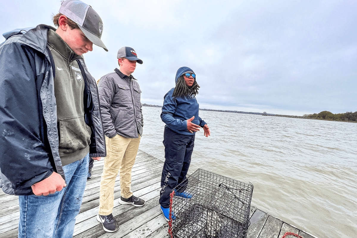 two teen boys standing on a dock with an instructor learning about large size commercial crabbing baskets