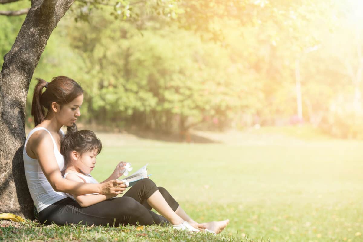 Mother and child read outdoors under a tree