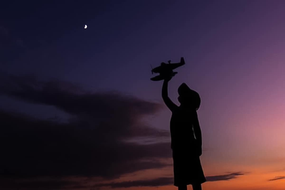 Silhouette of a child playing with an airplane under the night sky.