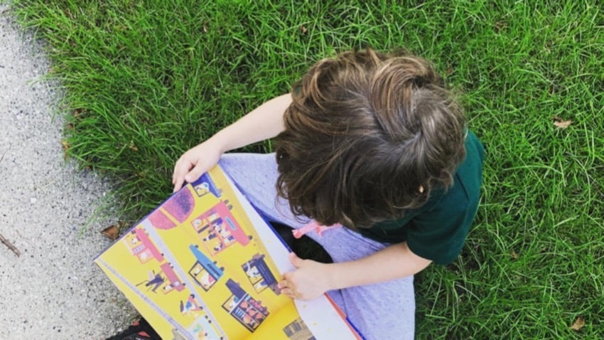 Child reading outside in the grass, seen from above
