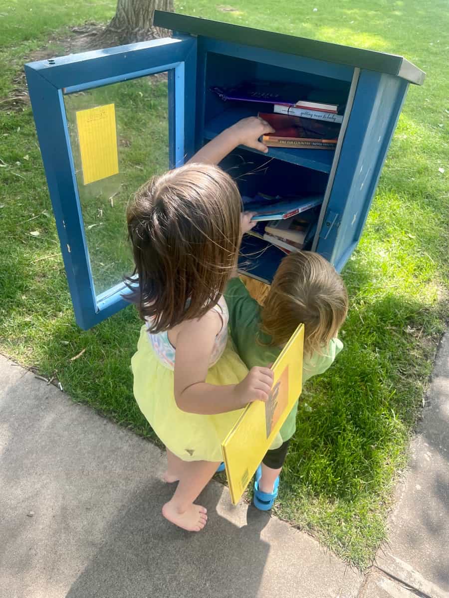 Two kids finding books in a Little Free Library at a park
