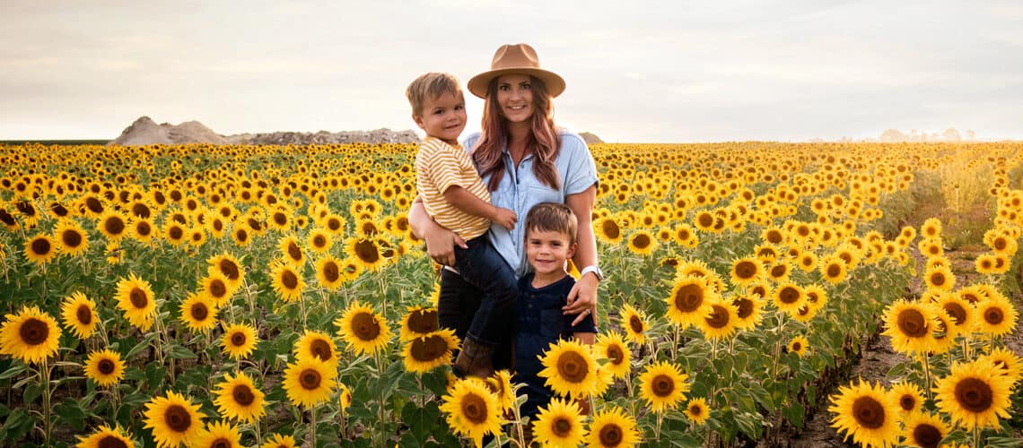 A woman and her children pose for a photo in a vast sunflower field.