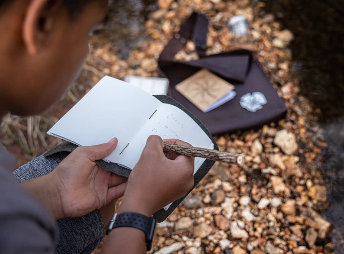 boy writing in notebook by creek
