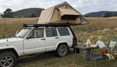 Two kids on a camp table with a rooftop tent.