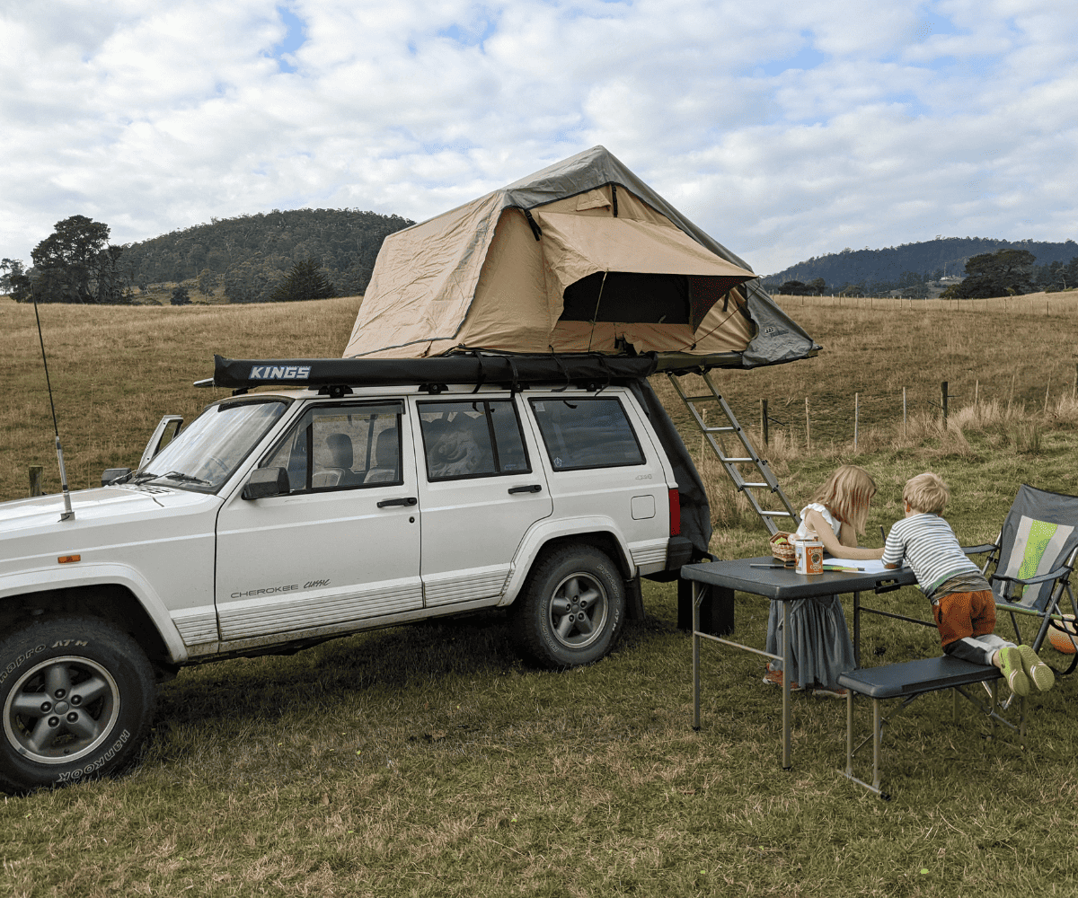 Two kids on a camp table with a rooftop tent. 