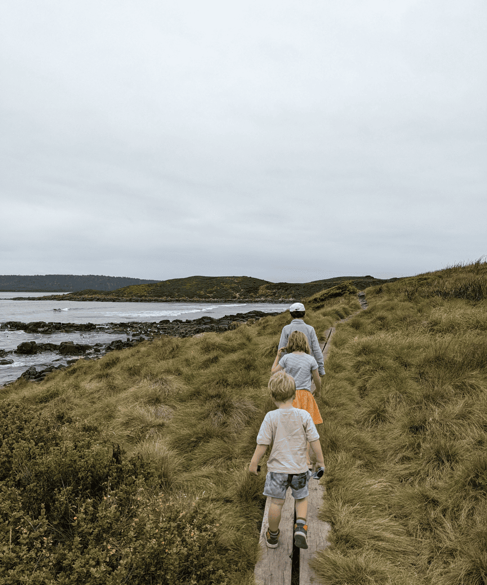 Three kids hiking on a boardwalk over the coastline