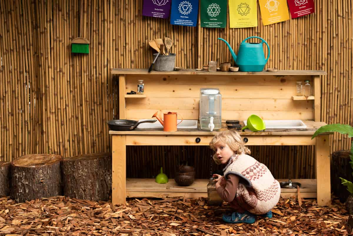 A child playing with mud and water in an outdoor mud kitchen.
