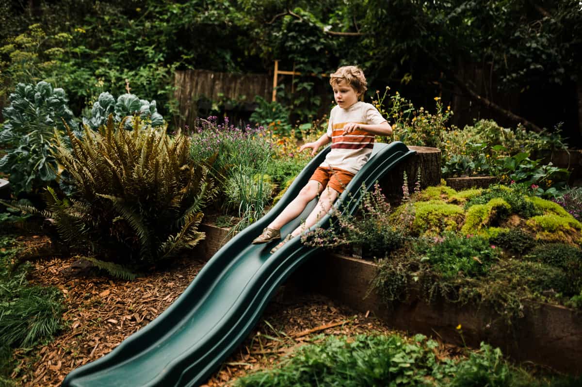 The ultimate guide to gardening with kids - child goes down sliding board in garden.