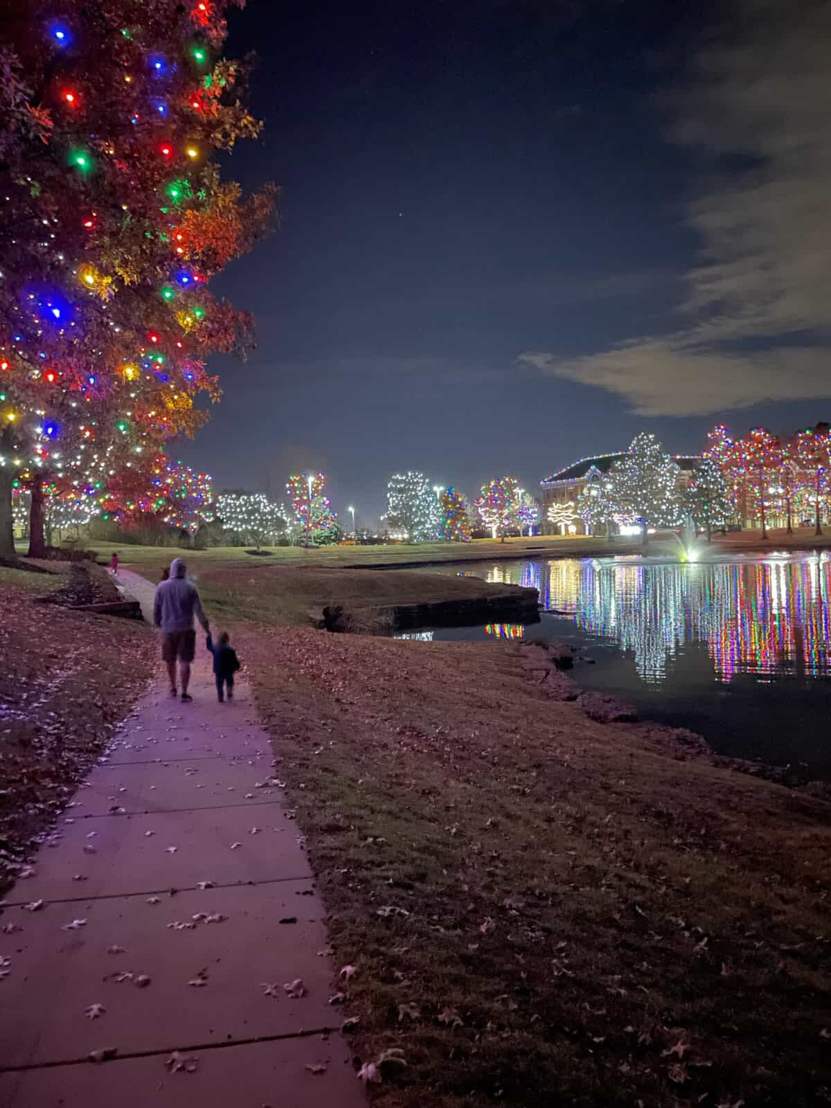 a man and child walking at night with Christmas Lights in the background 