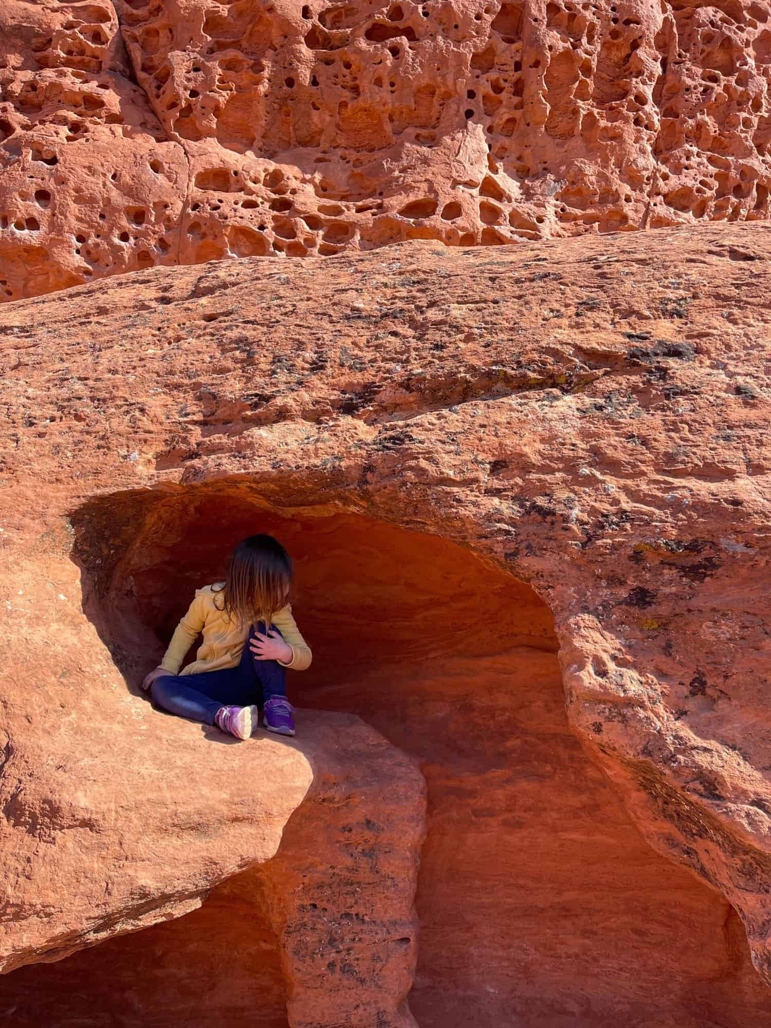 Child sitting in an alcove of some red rocks.