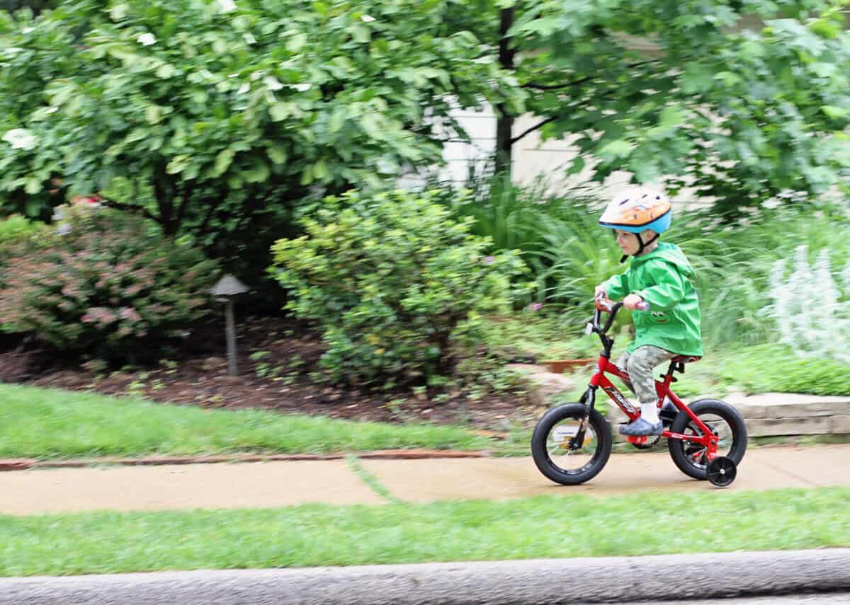 little boy in green rain coat riding bike with training wheels